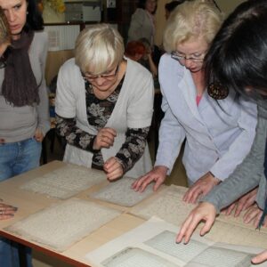 Skupiona nad rozłożonymi na stole przykładami tłoczeń pisma liniowego grupa odwiedzający Muzeum Tyflologiczne