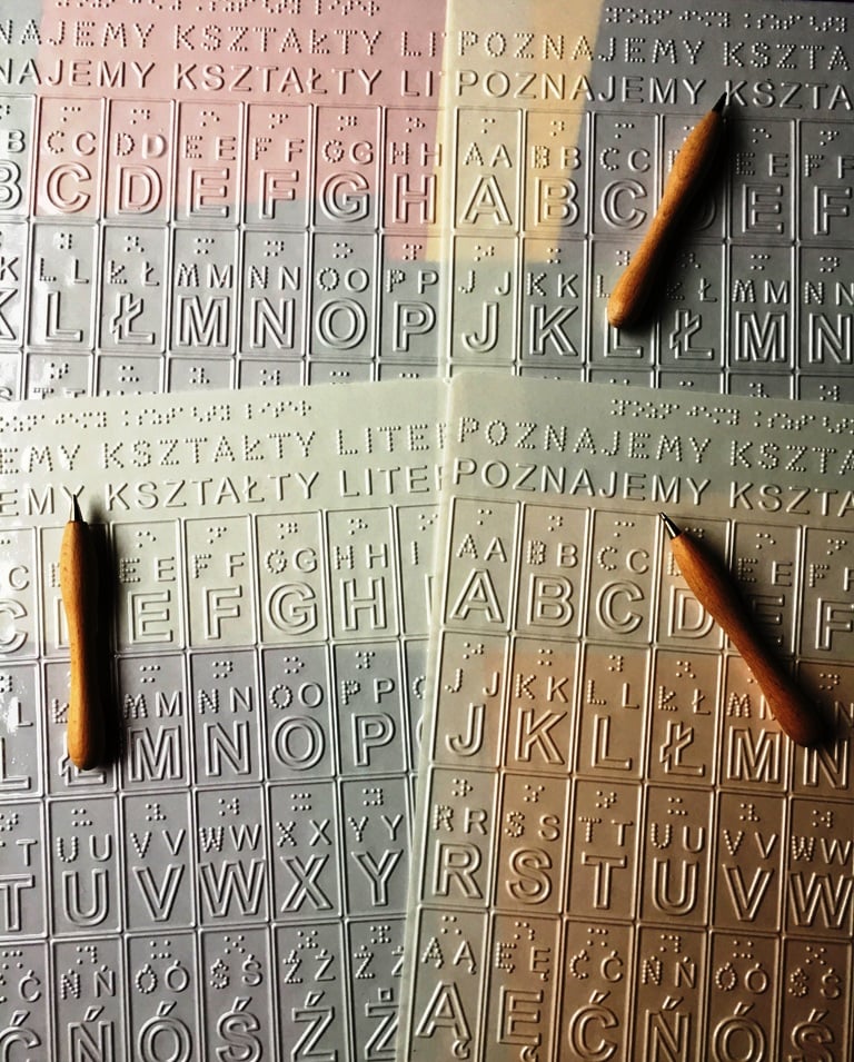 Cztery reliefowe planszety do poznawania kształtów liter widzących i ćwiczenia pamięci mechanicznej. Na białych arkuszach planszetów "kredki do rysowania"