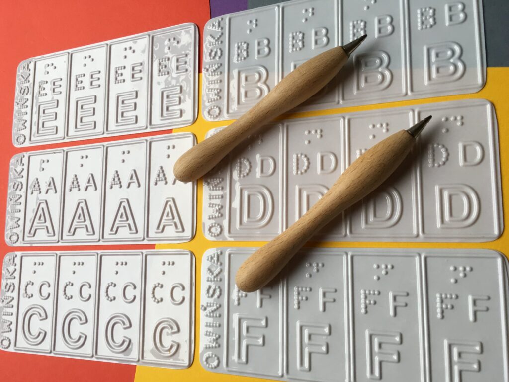 Tyflograficzne arkusze liter alfabetu łacińskiego do ćwiczenia pamięci mechanicznej wraz z dwoma kredkami do rysunku reliefowego.
