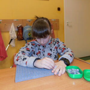 Dziewczynka na tle wieszaków w klasie szkolnej układa kostki kubarytmów w planszecie