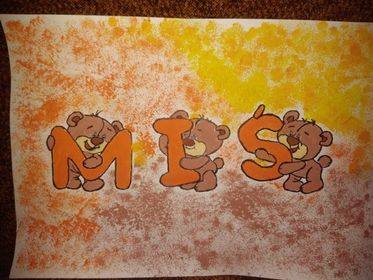 Praca plastyczna Łukasza. Na środku kartki widnieje napis MIŚ (każda litera trzymana jest przez misia). Literki pokolorowane są na pomarańczowo. Tło kartki postemplowane jest na żółto, pomarańczowo i brązowo.