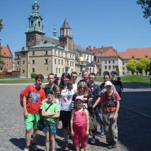 Grupa turystów na tle obiektów Wzgórza Wawelskiego. Słoneczny dzień i błękitne niebo.