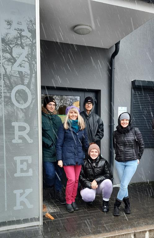 Przy wejściu do Schroniska stoi 5 osób: Martyna, Dominik, Damian, p. Marlena i p. Natalia. Pozują do zdjęcia w śniegowej pogodzie. Po lewej stronie duży napis AZOREK.