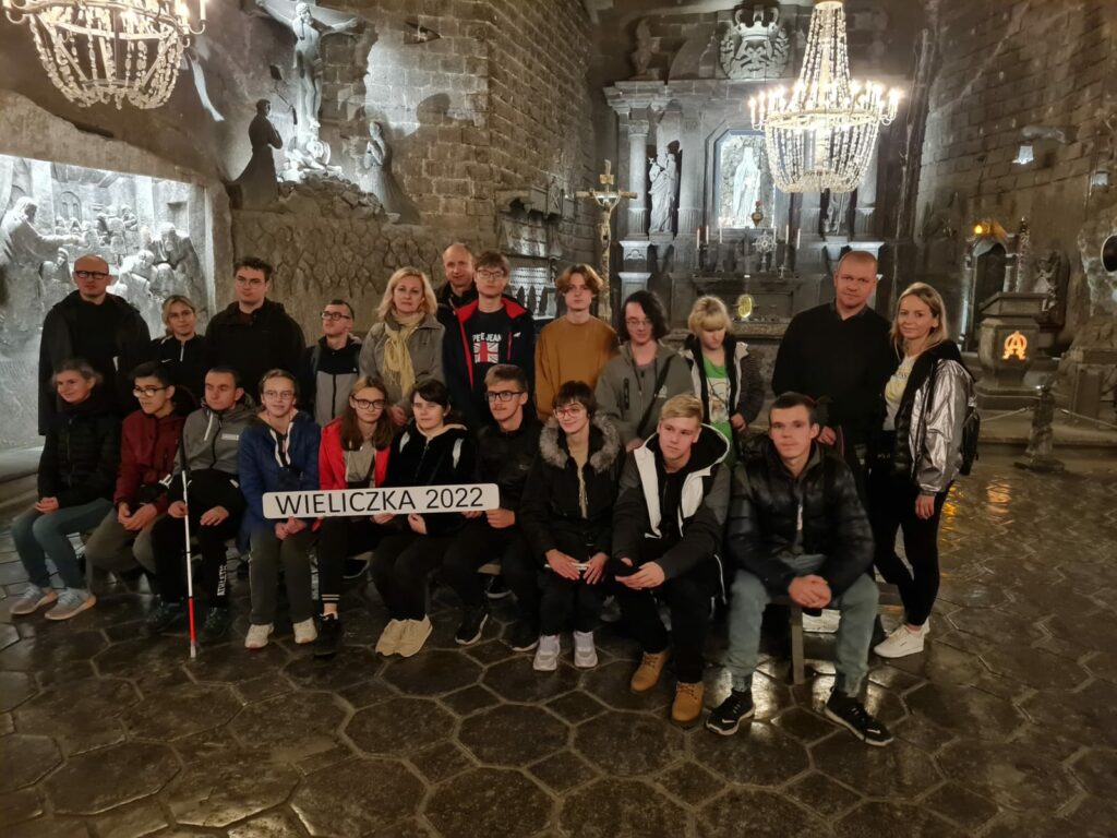 Grupa uczniów wraz z opiekunami w kopalni soli w Wieliczce. Zdjęcie zrobione na tle ołtarza w Kaplicy św. Kingi