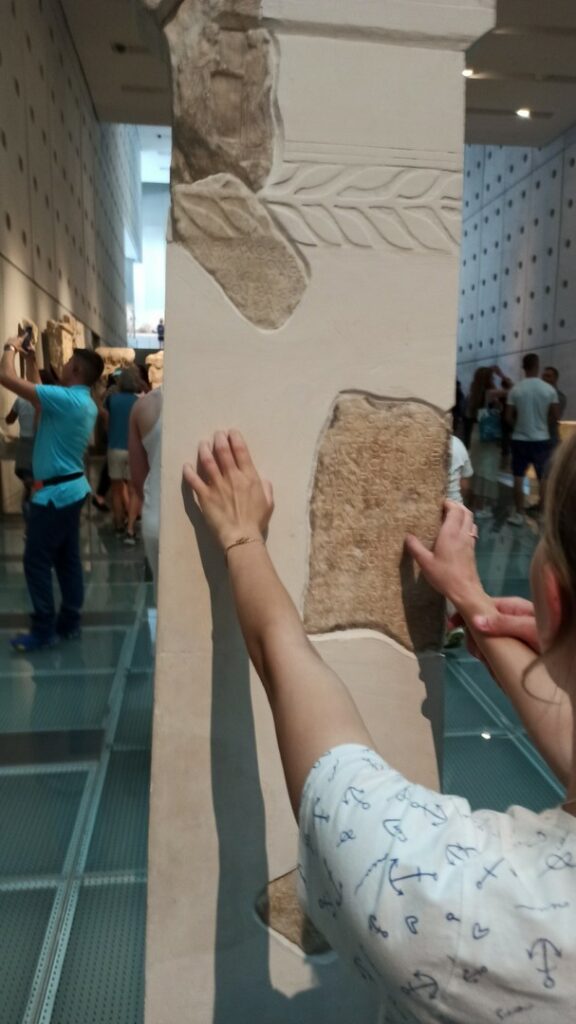 04. Inga stoi przed kolumną i ogląda dłońmi fragment odrestaurowanych ruin w muzeum Akropolu.