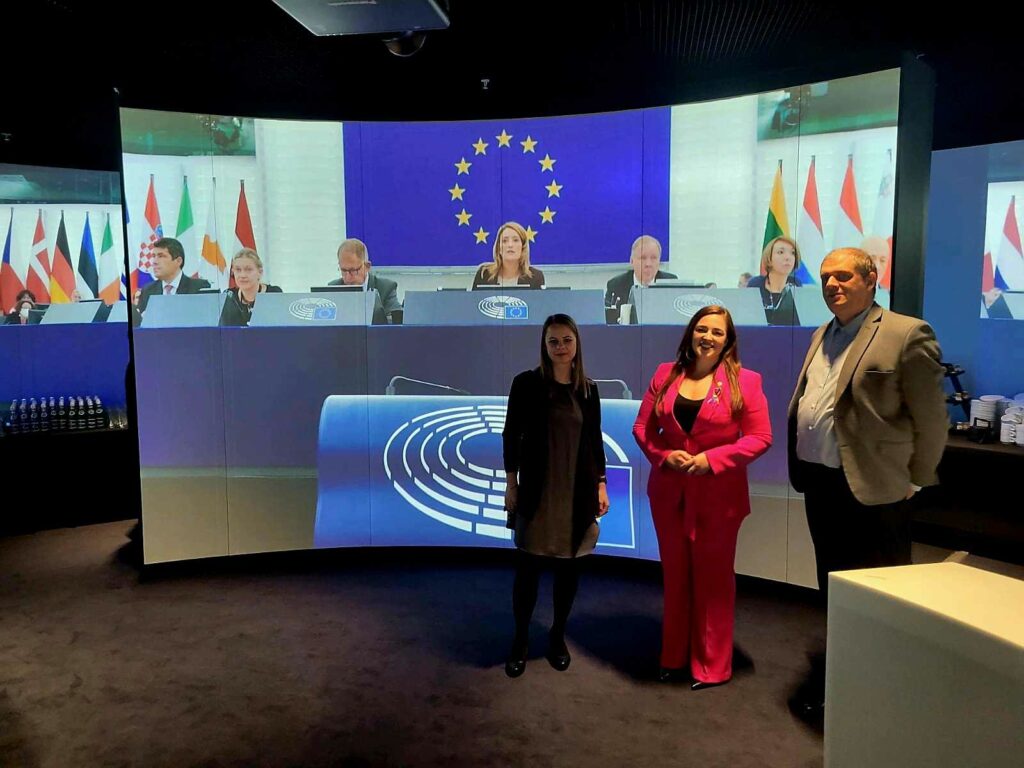 Na pierwszym planie od prawej Anna Szamotuła, Gabriela Jelonek i Dyrektor Bartłomiej Maternicki. W tle ekran z wyświetloną fotorgrafią konferencji UE i widoczną flagą UE.