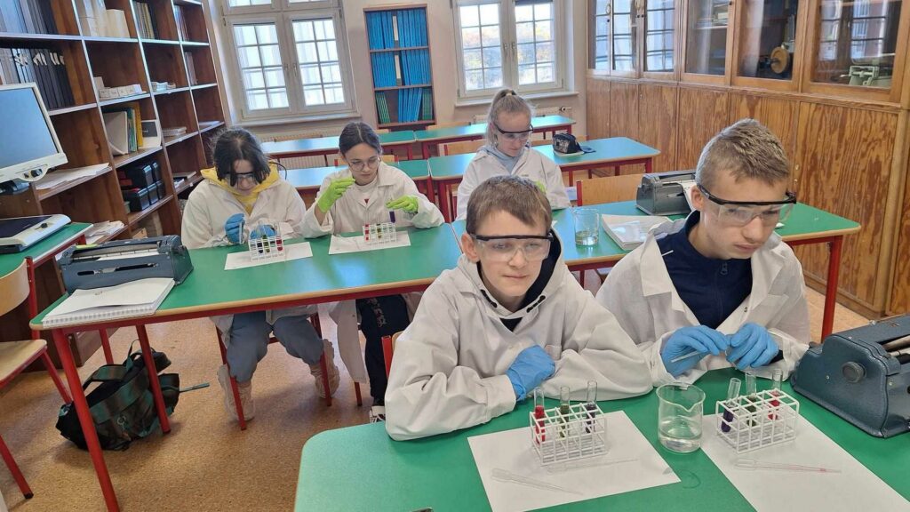 Uczennice w sali chemicznej wykonują eksperyment chemiczny i obserwują zachodzące zmiany. Od strony lewej: Kateryna, Alina, Wiktoria.y wskaźnik odczynu roztworu.